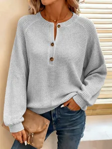 Close-up detail van een losse wafelgebreide top met lange mouwen en henley-knopen