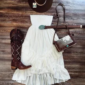White strapless tiered ruffle beach dress with western style accessories on wood background