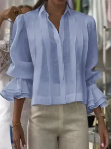Primer plano de una blusa plisada azul claro de manga larga con puños de volantes de doble capa
