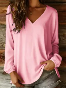 Detailed view of women's casual pink V-neck long sleeve blouse with rustic wooden wall backdrop