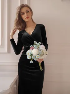 Elegant black velvet long-sleeved V-neck evening dress worn by a model in a studio setting.