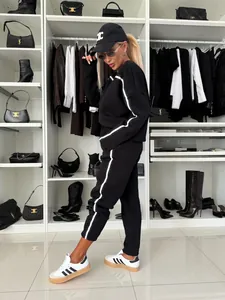 Model showcasing a black two-piece tracksuit with white stripes in a luxury walk-in closet