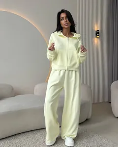 Full-length view of a woman wearing a pale yellow hooded cotton sweatshirt and wide-leg trousers.