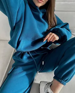 Woman wearing a stylish teal blue two-piece sports tracksuit set on a white sofa