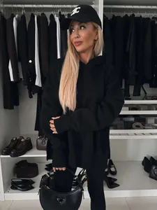 Mujer rubia posando con sudadera negra oversize y accesorios de lujo en el armario