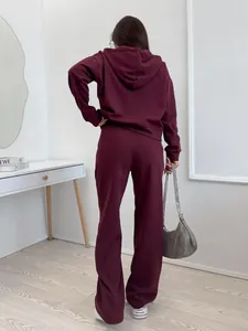 Back view of a woman wearing a burgundy solid color hooded tracksuit set in a room