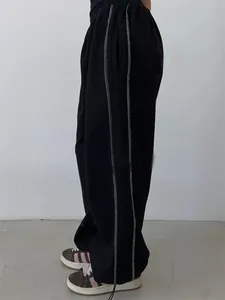 Side detail view of black baggy sweatpants featuring white contrast decorative stitching.