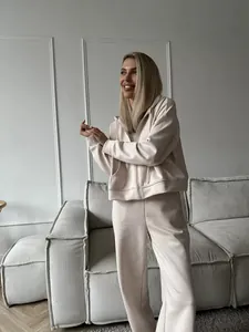 Woman wearing a stylish beige zip-up hoodie and pants set in a modern living room setting.