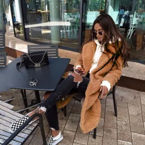 Femme à la mode portant un long manteau teddy marron dans un café de rue accueillant
