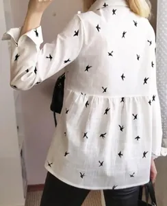 Detail view of the ruffled waist design on a white linen shirt with swallow print
