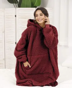 Woman wearing oversized burgundy sherpa wearable hoodie blanket in a cozy bedroom