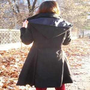 Detailed back view of a women's black hooded flared wool coat in an autumn setting.