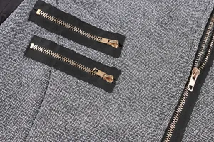 Close-up detail of golden zippers on grey textured woolen coat fabric with black accents.