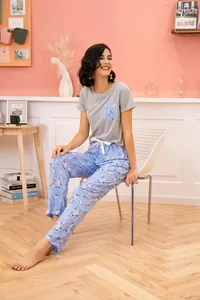 Woman wearing a grey short-sleeve top and floral blue pants in a cozy room setting.