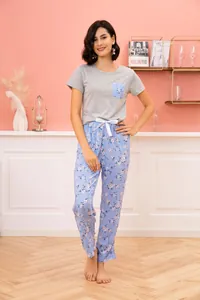 Model wearing grey short sleeve pajama top and blue floral pants in cozy home setting