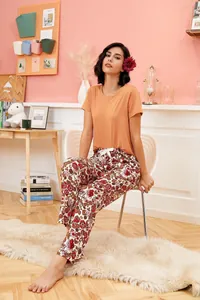 Women's two-piece pajama set with orange top and floral print pants in cozy room.