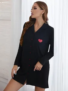 Détail de la chemise de nuit noire à manches longues avec imprimé cœur rouge sur la poche.