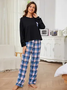 Women's black long sleeve pajama set featuring blue plaid pants in a cozy home setting
