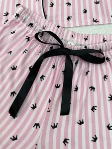 Détail d'un bas de pyjama rayé rose et blanc orné d'un nœud noir et de motifs couronnes