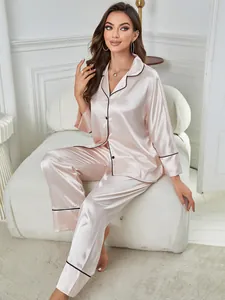Full view of an elegant pink silk satin pajama set with black piping in a cozy home setting.