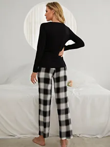 Back view of woman in black long sleeve top and black-white plaid pajama pants in bedroom.