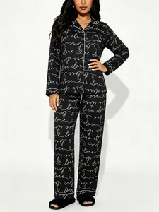 Model draagt zwarte pyjama met lange mouwen, witte Love-belettering en hartjespatroon.