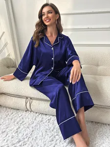 Detail view of navy blue satin pajama set with contrast white piping on a sofa