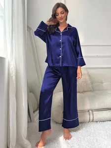 Elegantly posed model in a dark blue satin pajama set within a bright modern room.