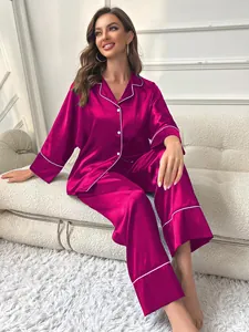 Elegant women's magenta satin long sleeve pajama set displayed on a white sofa