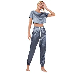 Model wearing grey satin two-piece pajama set with short crop top and jogger pants.