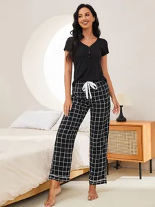 Woman wearing a black short-sleeve top and plaid pajama pants in a bedroom setting.