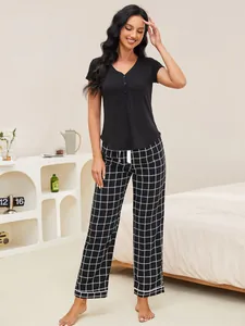 Elegant woman posing in black short sleeve pajama top and stylish grid print pants.