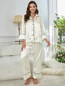 Woman wearing elegant cream satin pajama set with black piping in a cozy room setting