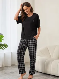 Detailansicht eines schwarzen Damen-Schlafanzugs mit Herz-Logo und schwarz-weißer Karo-Hose