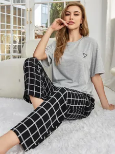 Ein Model trägt ein graues Kurzarm-T-Shirt mit Herz und eine karierte Schlafanzughose