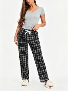 Full body view of a woman wearing a grey henley pajama top and black plaid long pants