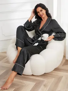 Elegant black satin pajamas with white piping worn by model in cozy armchair