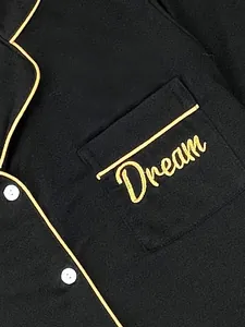 Detailopname van zwarte pyjamazak met goudkleurig Dream-borduurwerk en gele bies.