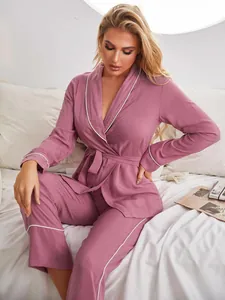 Dettaglio set pigiama rosa a maniche lunghe con profili bianchi indossato sul letto