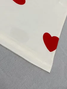 Close-up of the double-stitched hem and red heart print on a white cotton nightgown