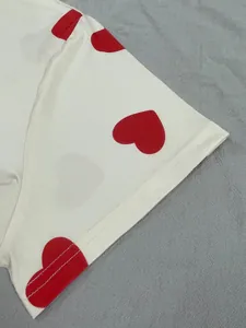 Close-up detail of red heart patterns and stitching on a white short sleeve pajama dress