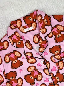 Close-up detail of pink women's satin pajama top featuring cute brown bear and heart print