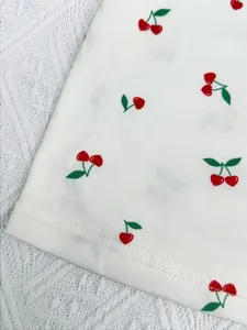 Close-up of white pajama fabric with red cherry prints and fine stitching detail.