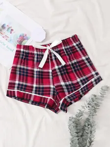 Detail view of red plaid pajama shorts featuring a decorative white bow and piping trim.