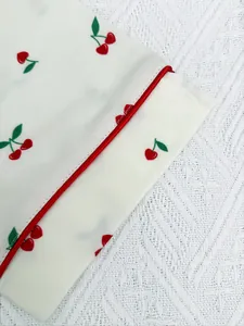 Close-up of soft white pajama fabric featuring red cherry prints and refined piped edges