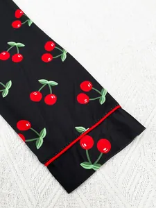 Close-up detail of cherry print on black pajama sleeve with red piping trim