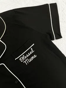 Gros plan du haut de pyjama noir pour femme avec broderie Blessed Mama et liseré blanc élégant