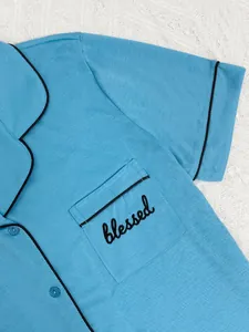 Détail du haut de pyjama bleu à manches courtes avec passepoil noir et broderie