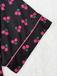 Détail d'un pyjama avec imprimé cerise et élégant passepoil rose sur tissu noir.