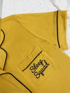 Λεπτομερές κοντινό πλάνο του κεντήματος Sleep Squad στην τσέπη της μουσταρδί πιτζάμας